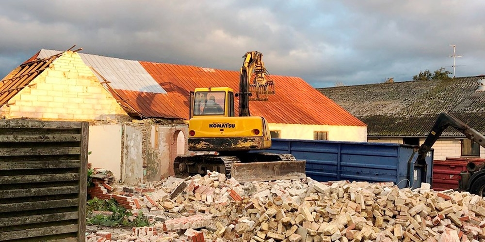 Maskine som er ved at udføre nedbrydning af et hus som var lavet ud af mursten.