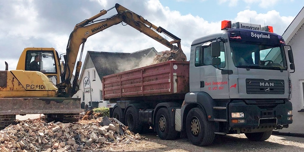 En maskine rydder byggeaffald op, over i en container på en lastbil.
